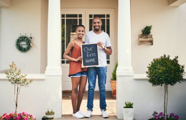Portrait of a young couple holding a chalkboard with our first home written on it.