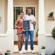 Portrait of a young couple holding a chalkboard with our first home written on it.