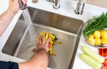 A hand shoves food waste into a disposer hole in the kitchen sink.