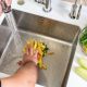 A hand shoves food waste into a disposer hole in the kitchen sink.