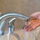 Woman taking a bath at home checking temperature touching running water with hand. Closeup on fingers under hot water out of a faucet of a sink or bathtub in house bathroom